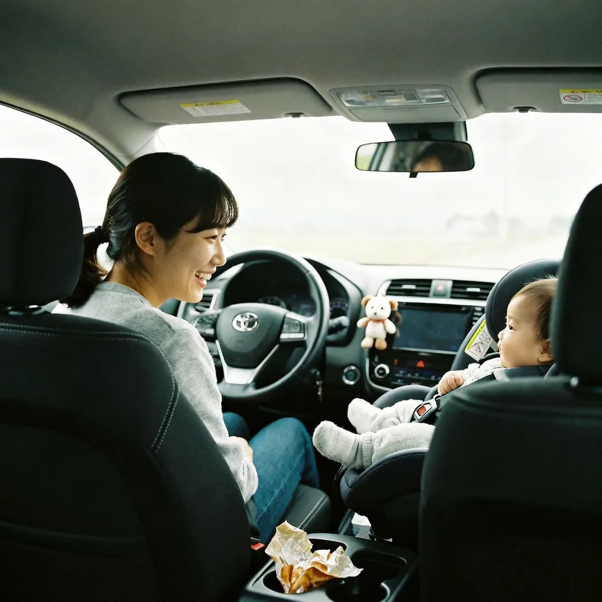 Mother smiling at baby in car seat during road trip with baby